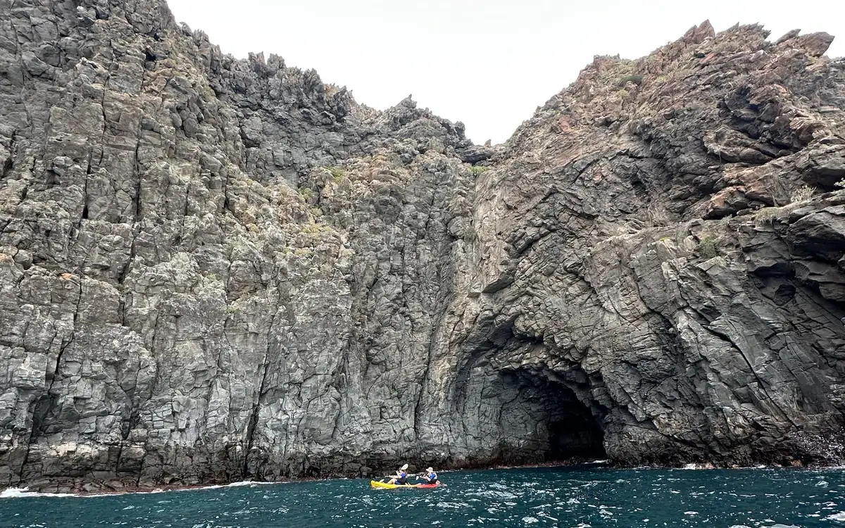 Two kayaks paddling towards a sea cave under tall dark cliffs