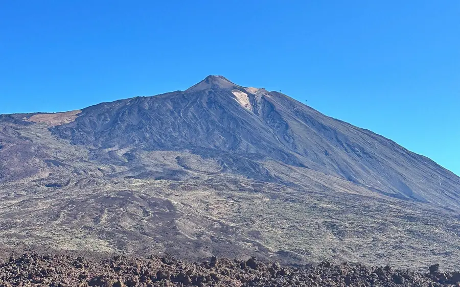 Mount Teide above a dark lava plain under a blue sky
