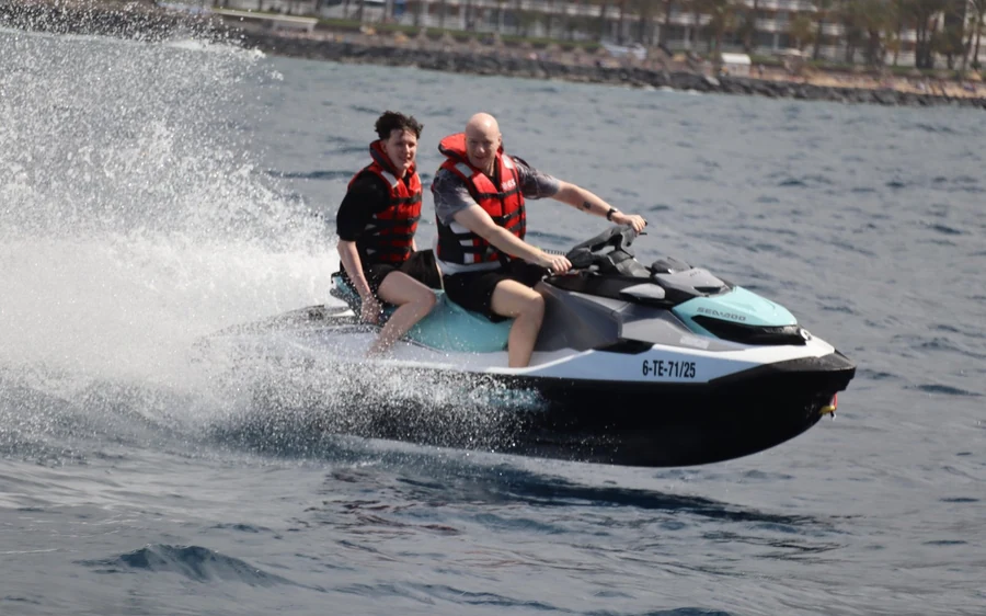 Two riders on a jet ski throwing up spray near the shore