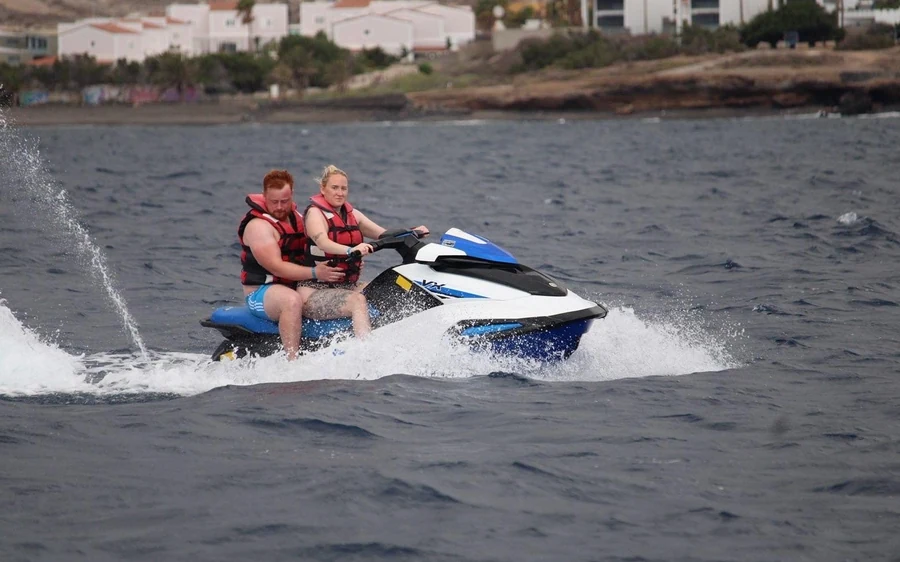 Two riders on a jet ski crossing grey water off the coast