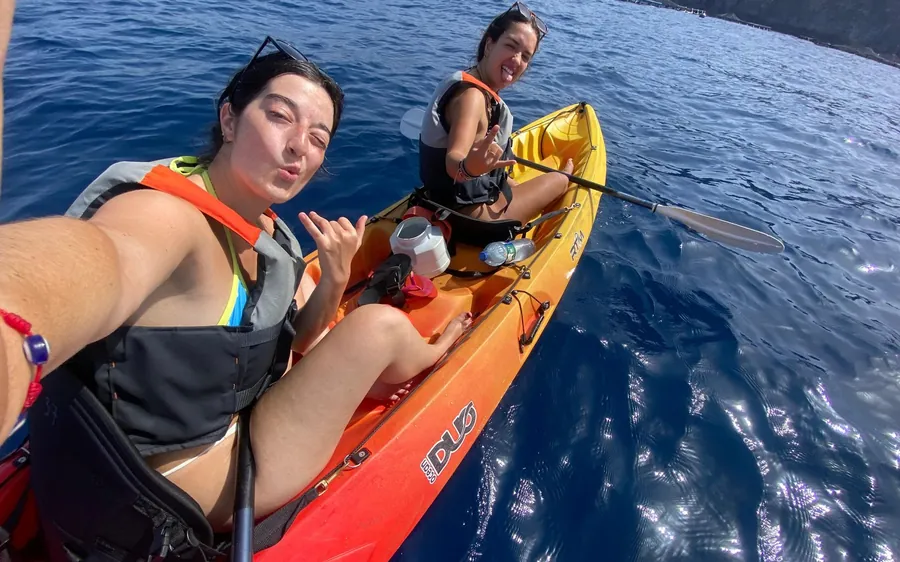 Two people paddling an orange sit-on-top kayak on blue water