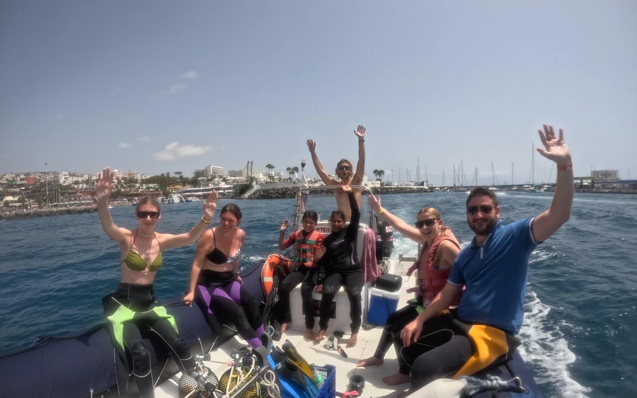 A group in wetsuits waving from an inflatable boat near a harbour